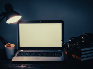 Laptop, headphones, table lamp, notebook, phone and flower at workplace. Distance work concept in quarantine. Modern freelance. Distance communication. Work in the evening.