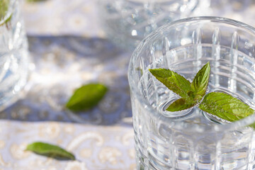 sprudelndes Wasser in einem durchsichtigen Glas mit einem Minzblatt auf einer gemusterten Tischdecke 