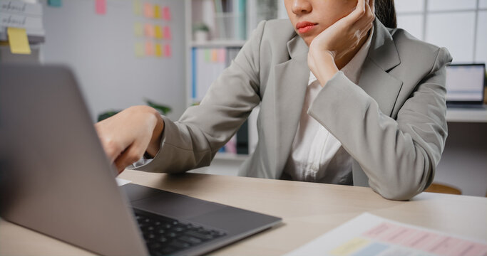Young Asian businesswoman sit on desk with laptop overworked tired burnout syndrome at office. Exhausted lady with sleeply eye at workplace, Girl not enjoy unhappy with work, Work mental health.