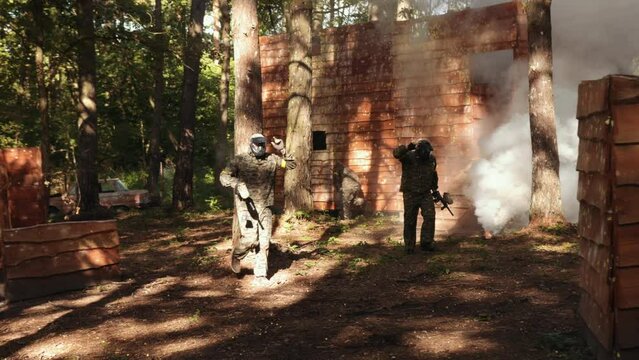 Playing paintball battles with his friends while wearing camouflage and protecting mask, an enjoyable leisure activity.