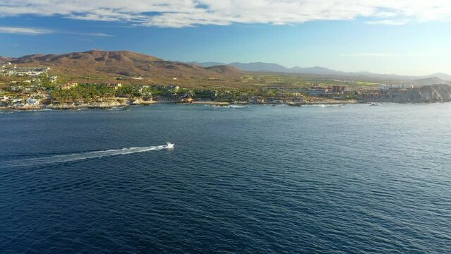 Aerial Shot Of Speedboat Moving On Sea By Hotels, Drone Flying Forward During Sunny Day - Cabo San Lucas, Mexico