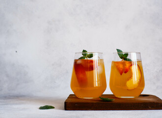 Two glasses of peach cocktail with ice, mint leaves on a gray background. Bar concept and summer drinks concept.
