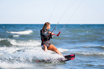 Kite surfing girl in swimsuit with kite in the sky rides the waves with splashing water. Water sports, sporty woman, action concept and hard sport