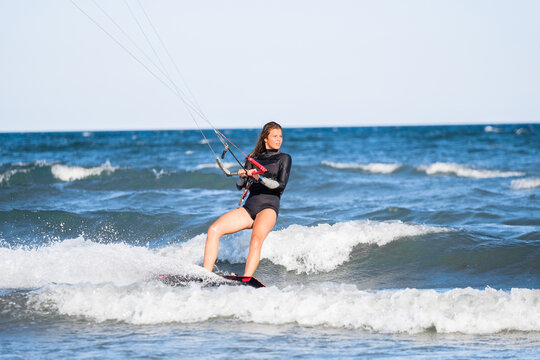 Kite surfing girl in swimsuit with kite in the sky rides the waves with splashing water. Water sports, sporty woman, action concept and hard sport