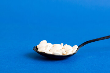 Heap of white pills on colored background. Tablets scattered on a table. Pile of red soft gelatin capsule. Vitamins and dietary supplements concept