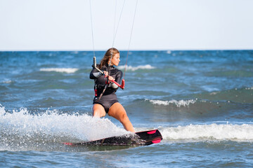 Kite surfing girl in swimsuit with kite in the sky rides the waves with splashing water. Water...