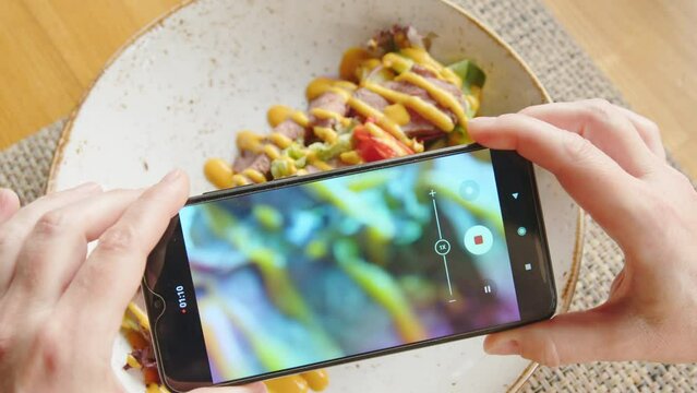 Female hands shooting food by smartphone closeup. Salad with meat and fresh vegetables seasoned with mustard sauce.