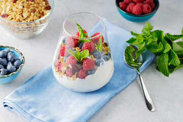 Healthy breakfast in glass of parfait. Yogurt with granola and berries on a blue napkin. Fresh raspberries and blueberries with homemade granola and yogurt