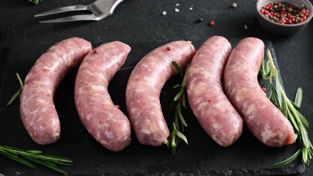 Bratwurst or raw pork sausages on dark background with rosemary and spices for cooking. Oktoberfest food. 4k video
