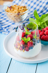 Healthy meal made of granola, yogurt and fruits on painted boards. Diet dessert with yogurt, granola and pomegranate fruit in a glass. Healthy breakfast on a blue surface