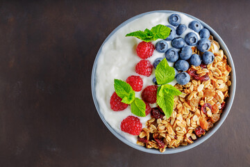 Granola with yogurt and berries on a dark brown background. Healthy breakfast with yogurt, baked granola, blueberries and raspberries. Top view. Copy space