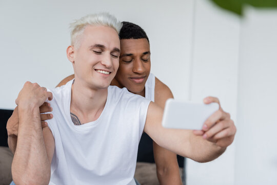 Multiethnic same sex couple taking selfie on smartphone at home