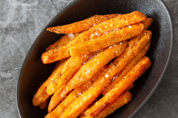 Sweet potato fries, seasoned with sea salt, in a black dish bowl.  On a dark stone background