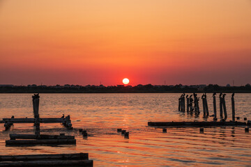 Fototapeta premium Beautiful red and orange sunset over the sea. The sun goes down over the sea. A flock of cormorants sits on a old sea pier in orange sunset light