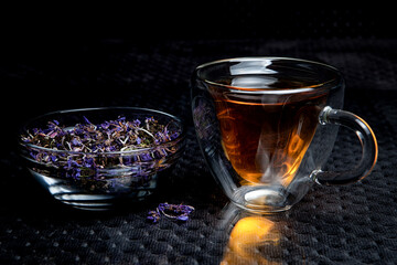 Homemade natural fermented tea with inclusions of blue Chamaenérion angustifolium flowers in a glass bowl on a black background next to a glass of tea.