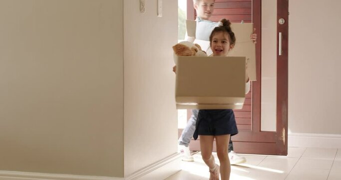 A family moving into their empty new home and carrying boxes while looking happy, excited and smiling. A mom, dad and carefree children holding packages as they enter their newly bought house.