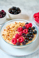 Oatmeal with raspberries, blackcurrants and crushed nuts in a glass bowl. Healthy balanced food