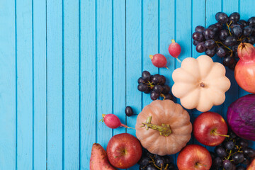 Autumn harvest concept. Pumpkin, apple and grapes on blue wooden background. Top view, flat lay