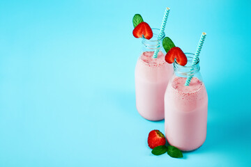 Strawberry smoothie or milkshake in glass jar with berries on blue background. Healthy summer drink
