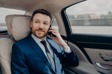 Young good looking businessman taking ride to conference while talking on phone