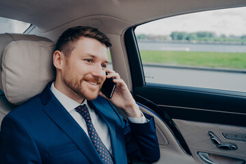 Attractive skilled banker in formal suit riding in corporate car and talking on cellphone