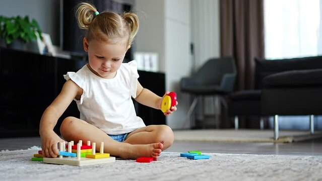Cute caucasian little girl playing on the floor at home with eco wooden toys. Montessori toy. The child playing educational games.