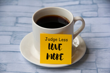 Inspirational quote text on yellow notepad on coffee cup - Judge less love more. Motivational...