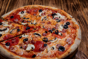 Tomato-based pizza with mozzarella cheese, hunting sausages, salami, olives, mushroom sauce. On a wooden background
