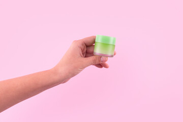 Female hand holding unbranded green plastic tube. Flacon for cream, toiletry. Bottle for professional cosmetics product. Skincare and beauty concept. Mockup, copy space. Isolated on pink.
