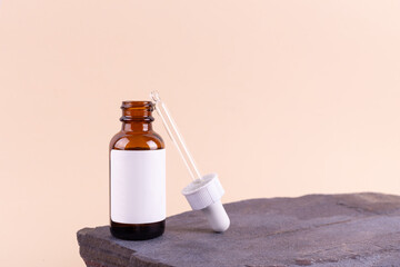 Unmarked amber glass bottle with dropper lid on beige background on the stone. Mock-up of facial serum in rays of sunlight. Close-up, copy space.