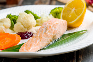 Salmon steak on steam with steamed egetables on old wooden table macro close up