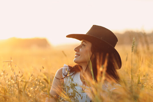 Woman farmer in cowboy hat profile portrait at agricultural field on sunset.