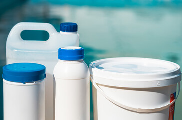 Close up photo of chemical cleaning products in bottles and bucket in front of the swimming pool