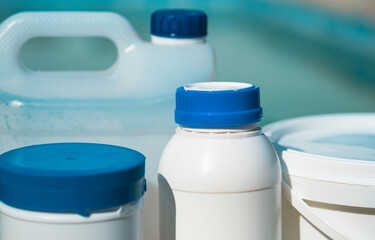 Close up photo of chemical cleaning products in bottles and bucket in front of the swimming pool