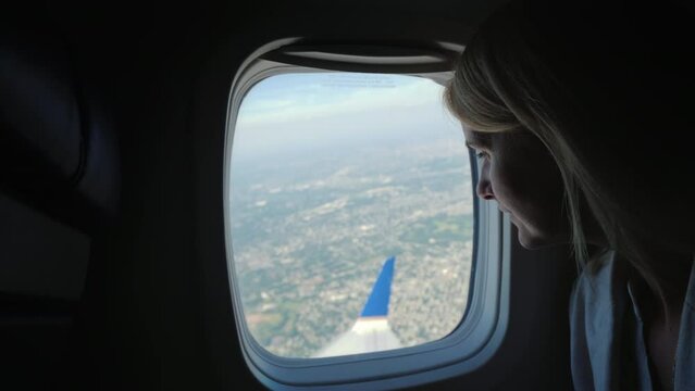 A young female passenger looks out of the window of the plane to the ground far below, where the metropolis is visible
