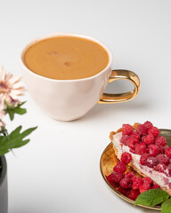 Cup of delicious coffee with blurry chrysanthemums and delicious piece of cake with fresh raspberries in the foreground. White background. Sweet concept.  Place for your text.