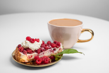 Delicious piece of cake with fresh raspberries and blurred cup of aromatic coffee in background. Blurred white background. Sweet concept. Excellent image for dessert banners and advertisements. 