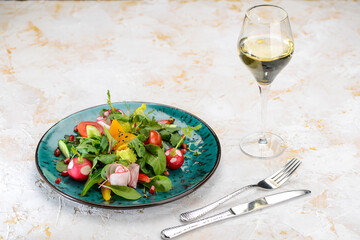 fresh salad with tomatoes spinach and radish in a blue plate on a white background with a glass of wine
