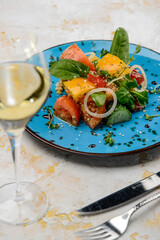 fresh salad with cucumber, lettuce and tomatoes in a blue plate on the table with a glass of wine vertical photo
