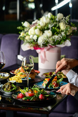 a table served with food in a restaurant with hands in the frame on a background of flowers
