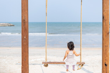 A girl sits on a swing and looks at the beautiful sea in the daytime on a rest day.