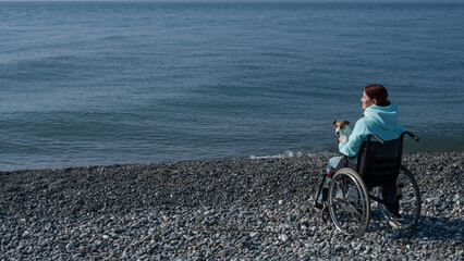 Obraz premium Caucasian woman in a wheelchair cuddling with a dog near the sea. 