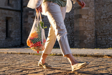 Woman walks on street and carrying reusable mesh bag with vegetable