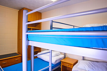 Empty dorm shared accommodation for adventure residential camping. Blue waterproof mattress, white pillows and quilt with no cover. - obrazy, fototapety, plakaty