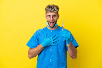 Dentist caucasian man holding tools isolated on yellow background surprised and shocked while looking right