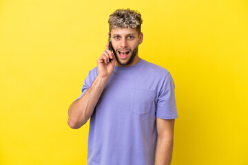 Fototapeta premium Young caucasian man using mobile phone isolated on yellow background with surprise facial expression