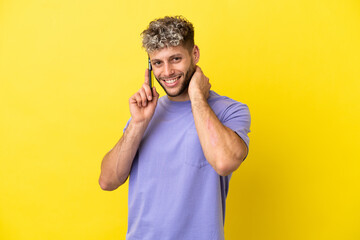 Young caucasian man using mobile phone isolated on yellow background laughing