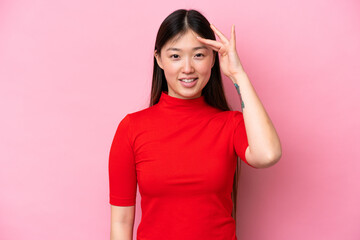 Obraz na płótnie Canvas Young Chinese woman isolated on pink background saluting with hand with happy expression