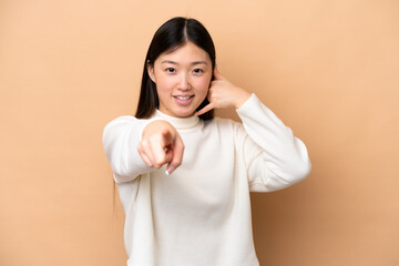 Young Chinese woman isolated on beige background making phone gesture and pointing front