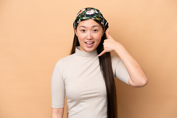 Young Chinese woman isolated on beige background making phone gesture. Call me back sign